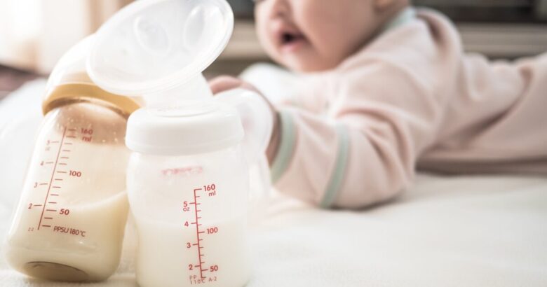 bebé tumbado al fondo mientras un sacaleches eléctrico y varios biberones con leche materna extraída aparecen